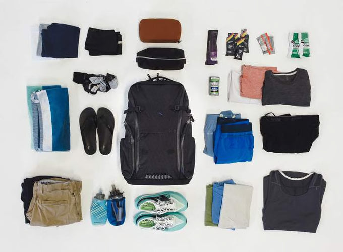 A DVRGE backpack surrounded by must-have items for international travel for athletic events, including clothes, toiletries, and sports gear.