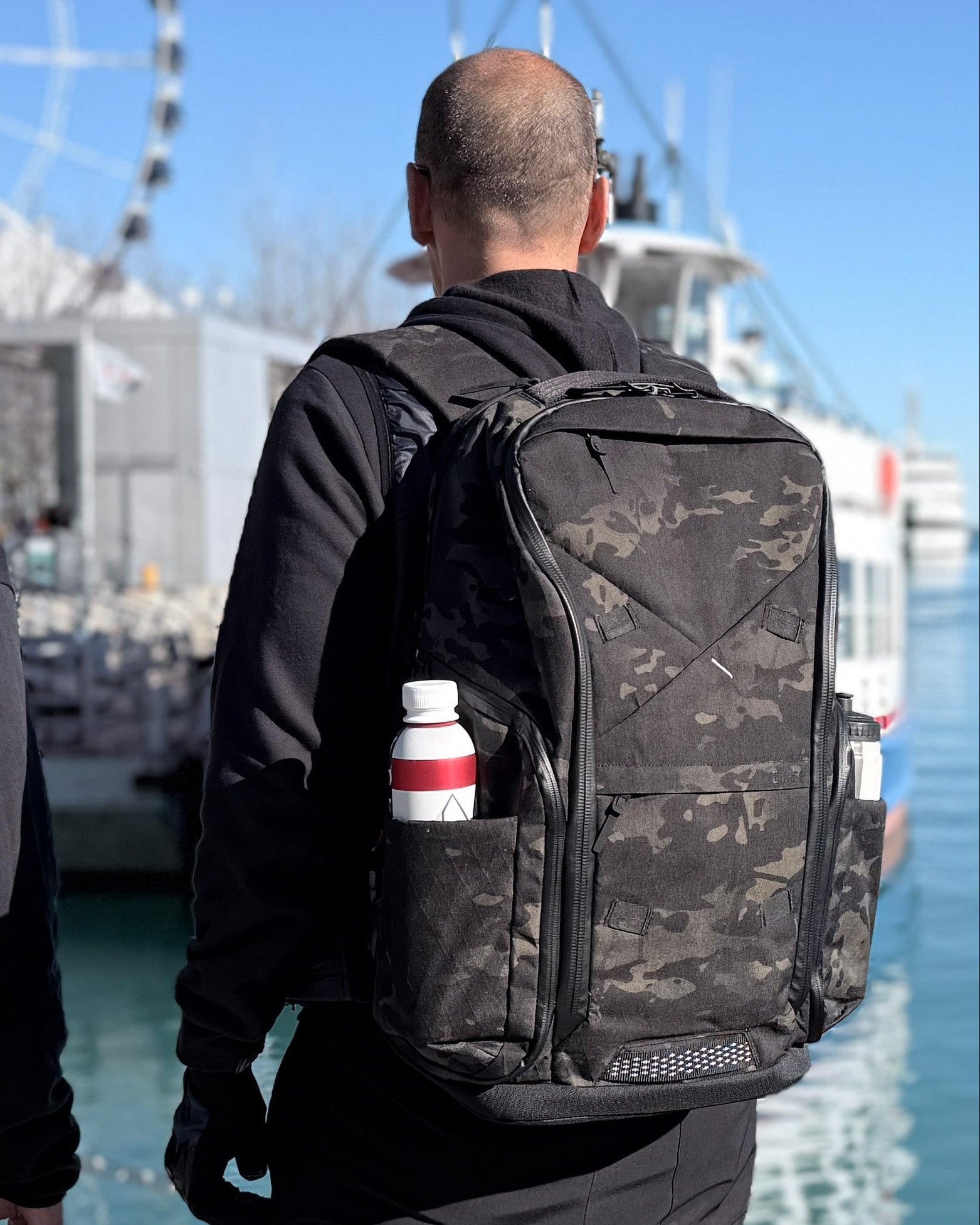 A man wears the DVRGE X50 36L – Waterproof X-Pac® X50 Black Multicam® - LIMITED EDITION backpack while looking out over the pier