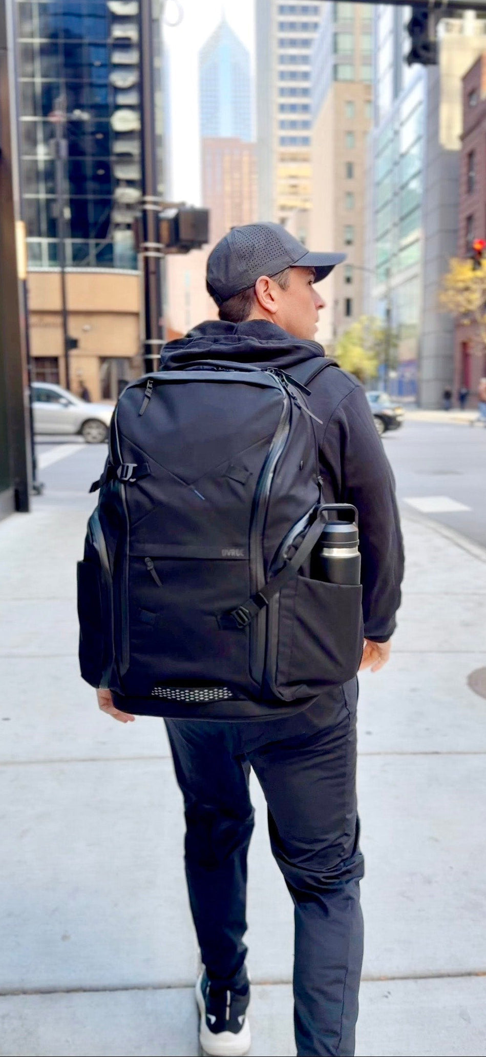 Owner of DVRGE walks away from the camera toward a cityscape carrying his DVRGW carryon backpack