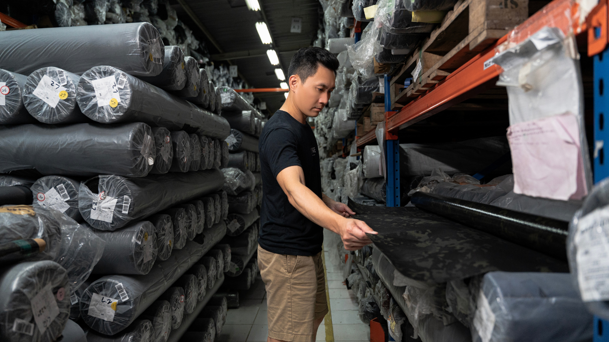 Andy in X PAC warehouse, examining stacks of black rolls of material.