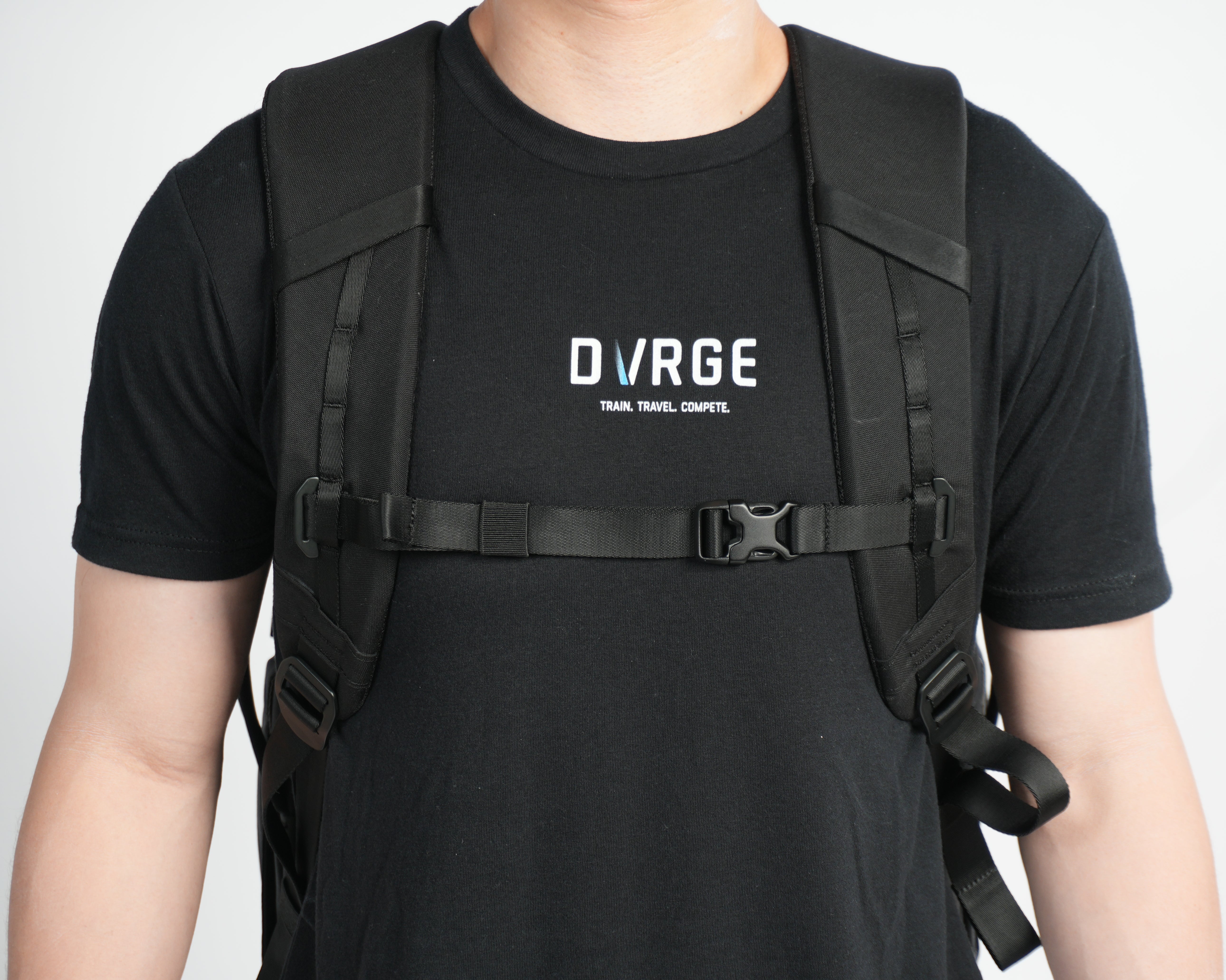 Person wearing a black t-shirt with 'DURGE' logo and a black backpack on a white background, demonstrating adjustable chest strap