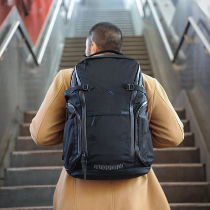 Person with a black backpack walking up stairs in an urban setting
