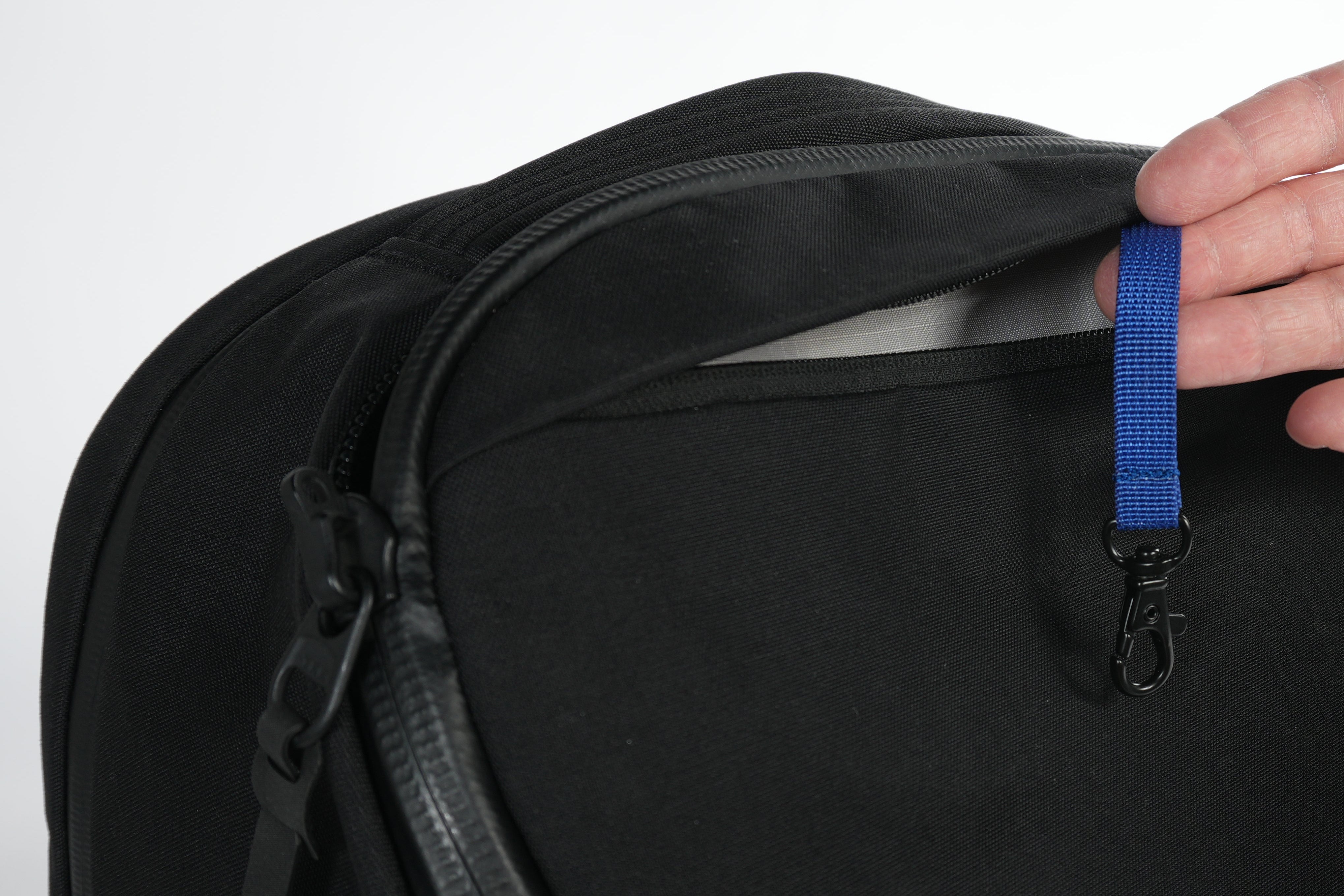 Black backpack with a blue key leash displayed by a hand on a white background